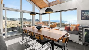 A modern kitchen with large windows, a wooden dining table, and a view of the ocean.