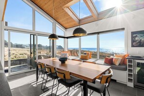 A modern kitchen with large windows, a wooden dining table, and a view of the ocean.