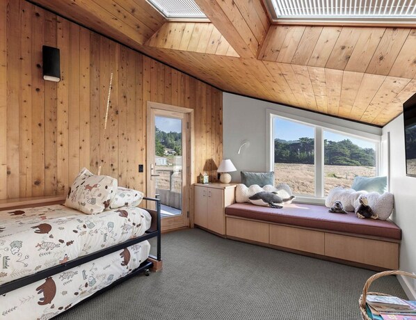 A room with wooden walls, a bed with animal-themed bedding, a window seat with cushions, and a skylight.