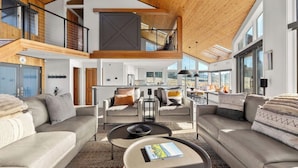 A spacious living area with a high ceiling, a mezzanine level, and large windows.