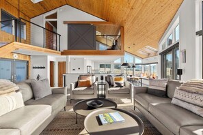 A spacious living area with a high ceiling, a mezzanine level, and large windows.
