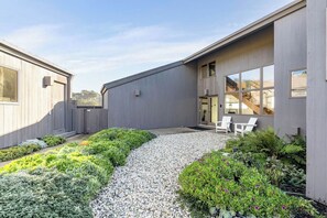 Un bâtiment moderne doté d’un chemin de gravier, d’un espace extérieur aménagé pour s’asseoir et d’une végétation luxuriante.