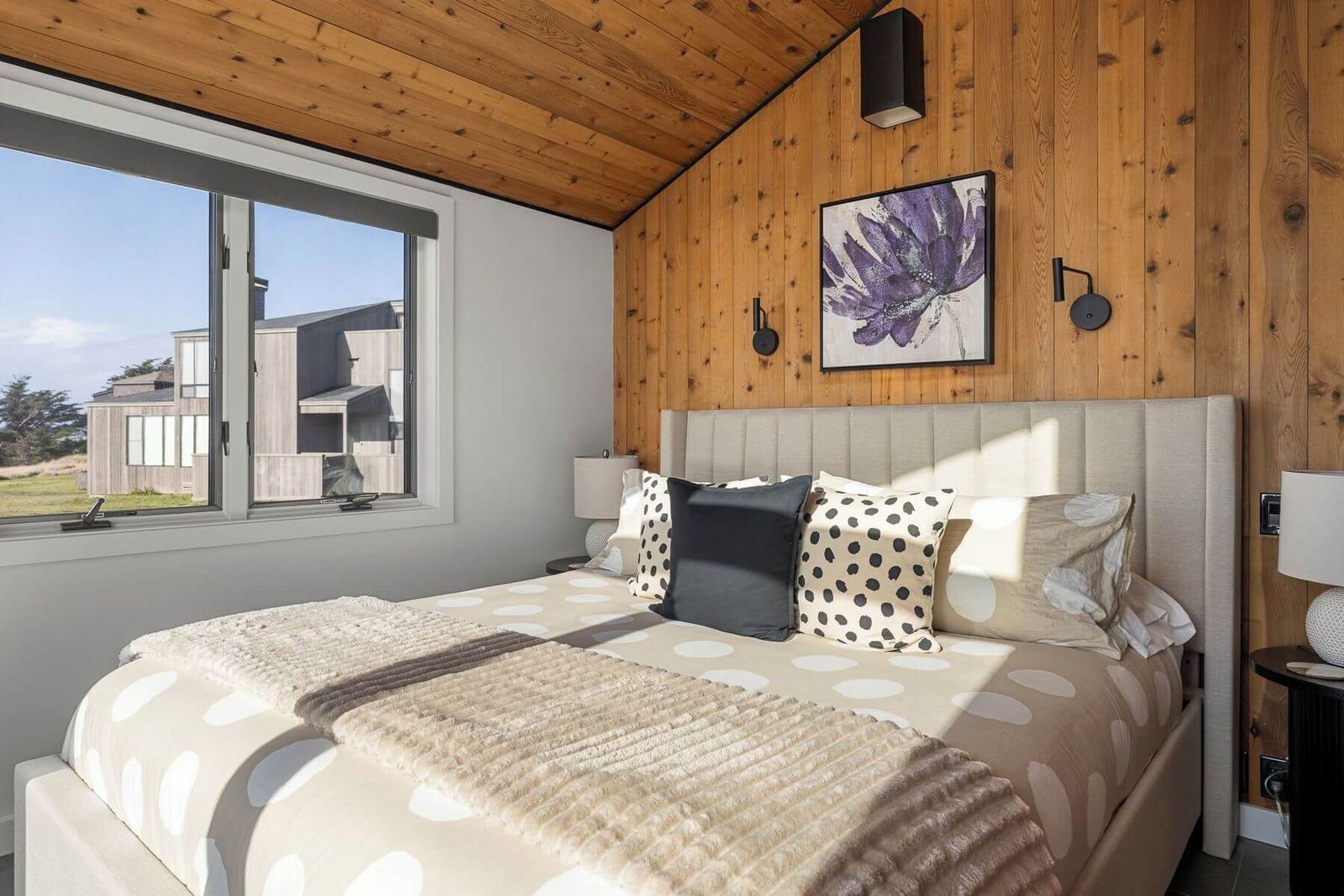 A bedroom with a large bed, a window, wooden walls, and a ceiling light.