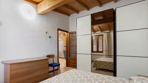 Una camera da letto con un comò in legno, un letto con copriletto decorato, una sedia e un armadio con ante scorrevoli.