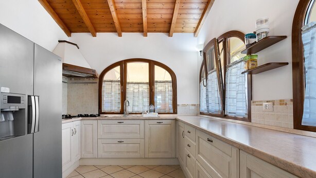 Cucina con frigorifero in acciaio inossidabile, mobili bianchi, pavimento piastrellato e soffitto in legno.