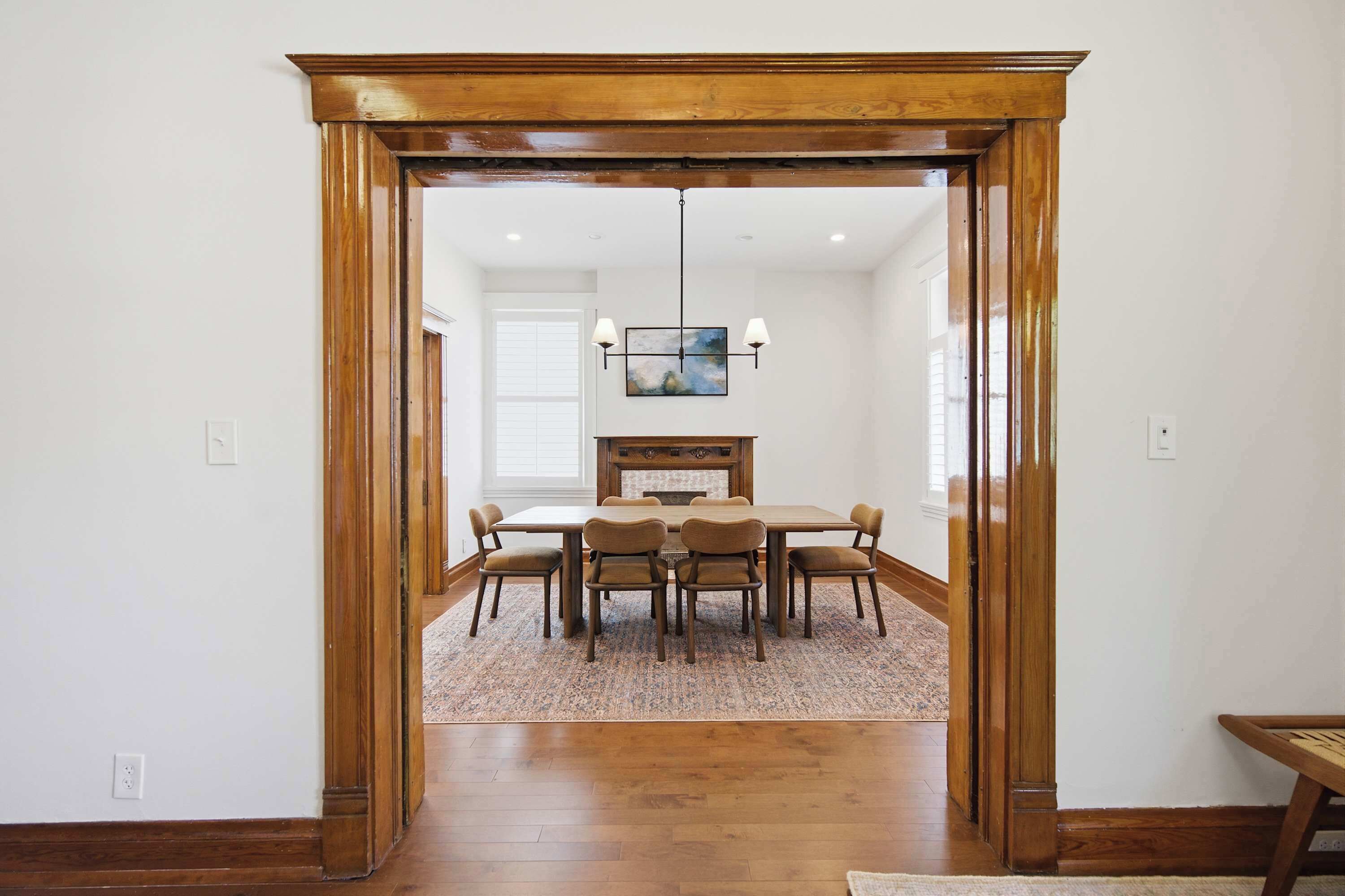 A dining area with a wooden table and chairs, a rug, and a chandelier.