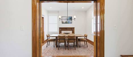 A dining area with a wooden table and chairs, a rug, and a chandelier.