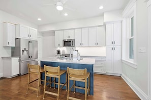 A modern kitchen with white cabinetry, a stainless steel refrigerator, a microwave, and a blue island with bar stools. - Hillside Hyde Park Home 4bdr (Cincinnati)
