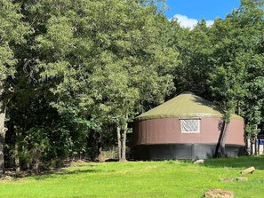 A yurt with a brown exterior and a green roof, surrounded by a grassy area and trees. - Luxury Yurt Near Fort Smith Hot Tub, Fishing Pond, & Hiking (Greenwood)