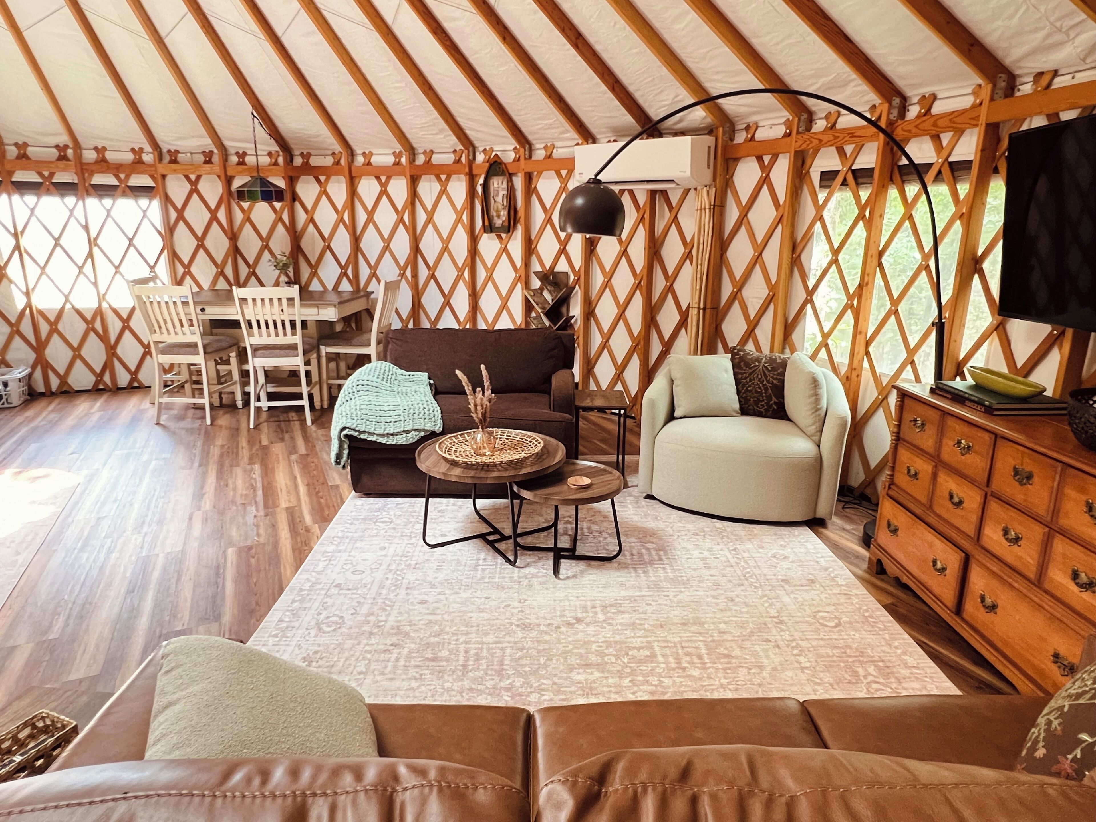 A tented accommodation with a dining area, sofas, a TV, and a wooden cabinet.