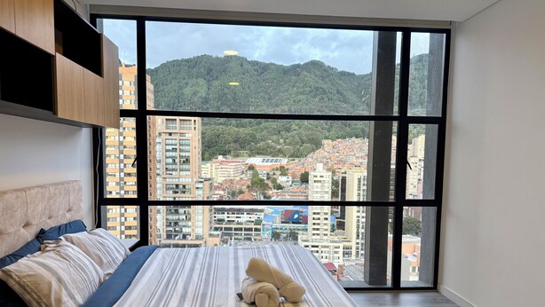 Una camera da letto con un'ampia finestra, un letto con lenzuola a righe e un orsetto sul letto.