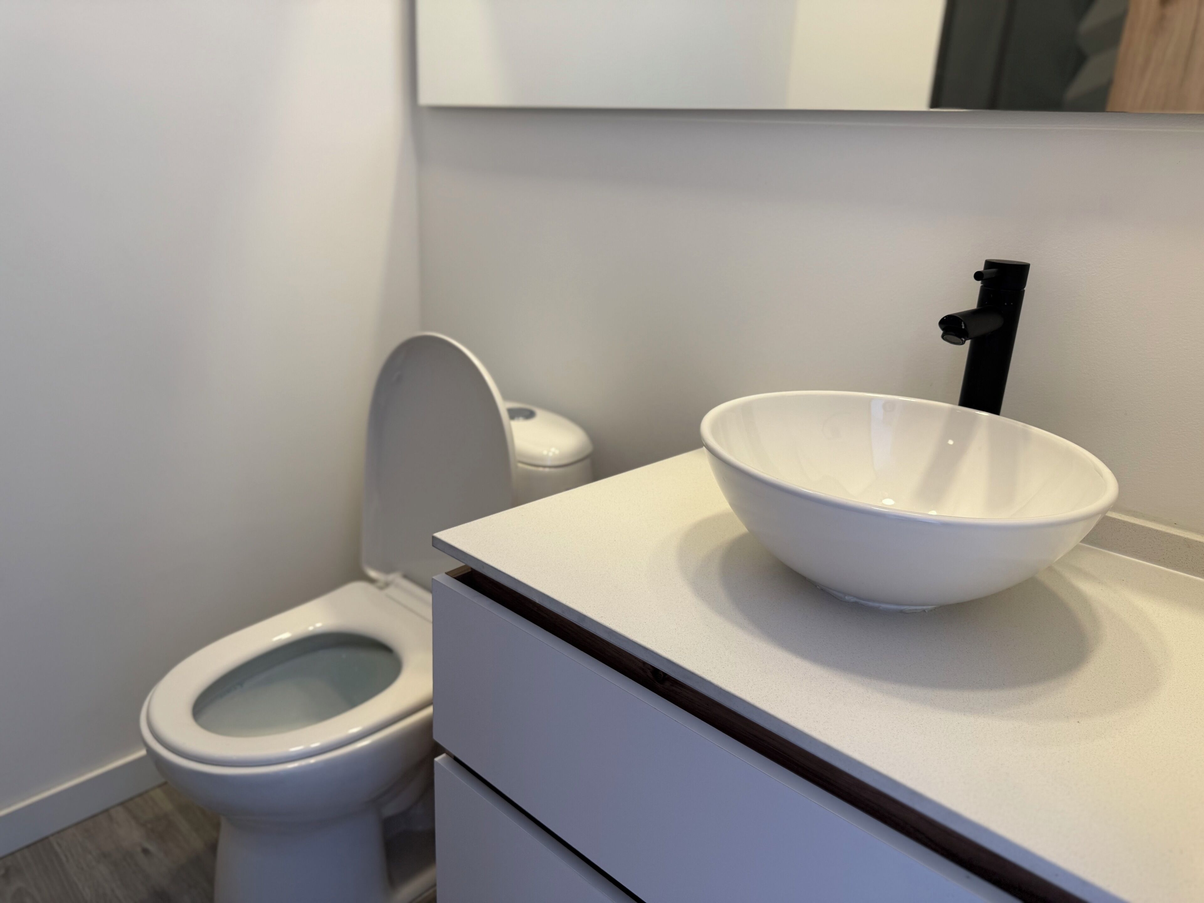 A modern bathroom with a white toilet, a white sink with a black faucet, and a white cabinet above the sink.