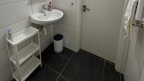 Een badkamer met witte betegelde wanden, een witte wastafel met spiegel erboven, een witte handdoekhouder en een witte deur.