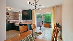 Una cocina moderna con armarios verde oscuro, una mesa de comedor de madera con sillas, y un ventanal con cortinas.