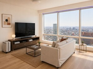 Ein modernes Wohnzimmer mit großem Fernseher, einer Couch, einem Couchtisch und einem großen Fenster mit Blick auf die Stadt.