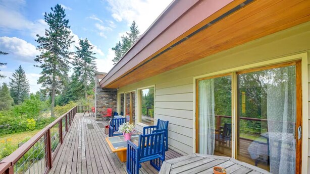 A wooden deck with outdoor furniture, a stone wall, and a view of trees. - Majestic Sandpoint Rural Retreat-Enclosed Acre, Min's to town & Schweitzer-! (Sandpoint)