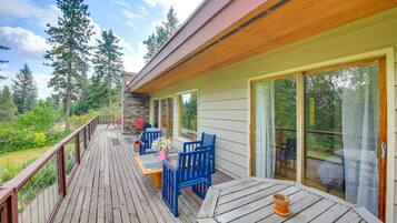 A wooden deck with outdoor furniture, a stone wall, and a view of trees.