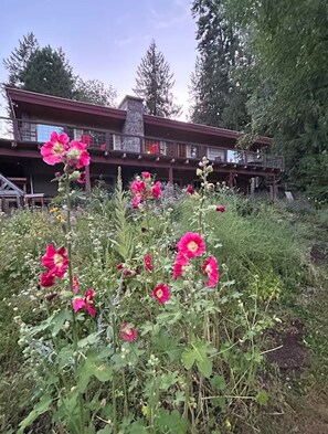 Een gebouw met een stenen schoorsteen, een balkon en een tuin met roze bloemen.