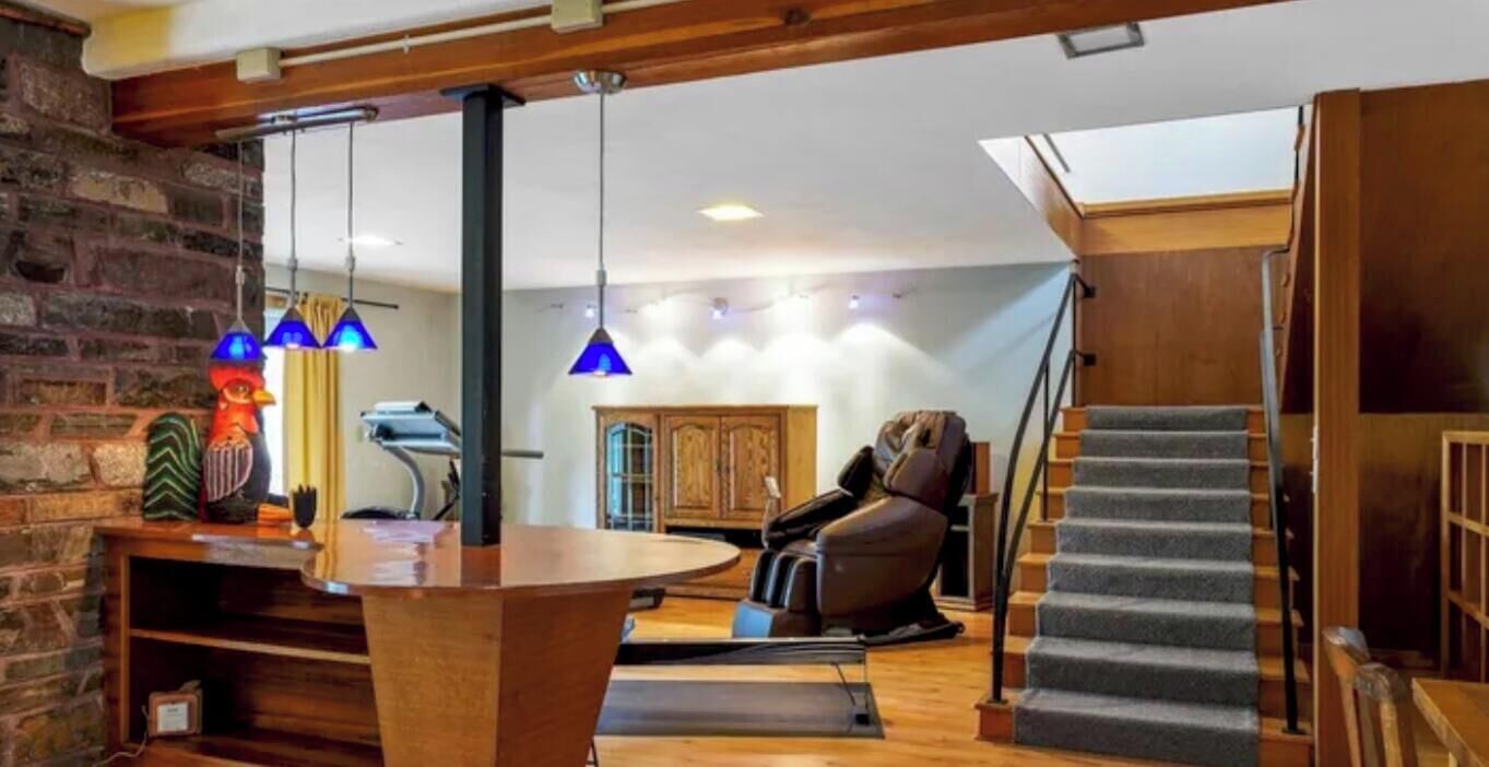 A modern living room with a stone wall, a massage chair, a wooden table, and a staircase.
