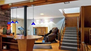 A modern living room with a stone wall, a massage chair, a wooden table, and a staircase. - Majestic Sandpoint Rural Retreat-Enclosed Acre, Min's to town & Schweitzer-! (Sandpoint)