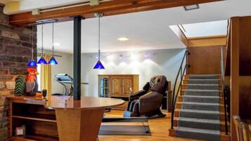 A modern living room with a stone wall, a massage chair, a wooden table, and a staircase.