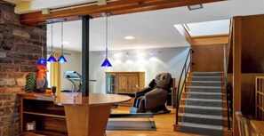 Uma sala de estar moderna com uma parede de pedra, uma poltrona de massagem, uma mesa de madeira e uma escada.