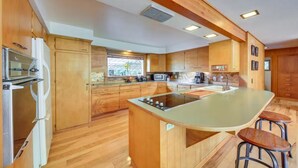 A modern kitchen with wooden cabinets, a central island, bar stools, and built-in appliances. - Majestic Sandpoint Rural Retreat-Enclosed Acre, Min's to town & Schweitzer-! (Sandpoint)