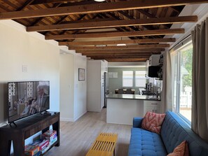 Ein Wohnzimmer mit Fernseher, Sofa, Couchtisch aus Holz und einer Küche im Hintergrund.