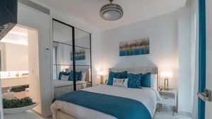 Ein modernes Hotelzimmer mit einem großen Bett, Nachttischen, einem Spiegel und einem Kunstwerk an der Wand.