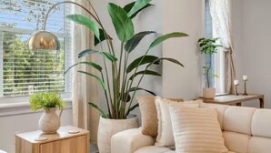 A living room with a sofa, a side table, a potted plant, and a window with blinds. - 30A Escape at 29 Blue Eden Loop (Santa Rosa Beach)