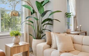 A living room with a sofa, a side table, a potted plant, and a window with blinds. - 30A Escape at 29 Blue Eden Loop (Santa Rosa Beach)