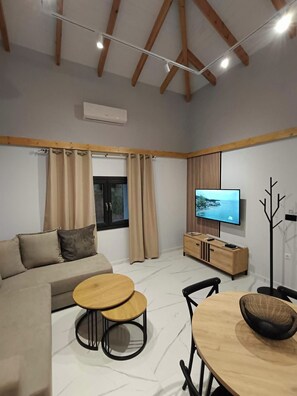 A modern living room with a sofa, two round tables, a TV, and a coat rack.
