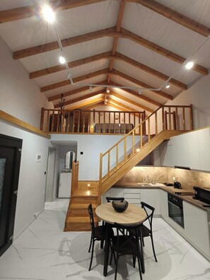 A spacious loft-style kitchen with a wooden staircase, a dining area with a round table, and a view of the upper loft.