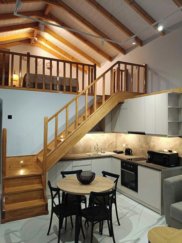 Una cocina moderna con una escalera de madera, un comedor con una mesa redonda y sillas, y un horno empotrado.