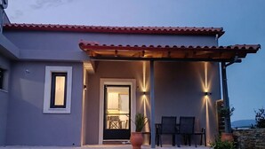 Una casa moderna con techo de tejas rojas, una entrada bien iluminada y un pequeño patio con sillas y una mesa.