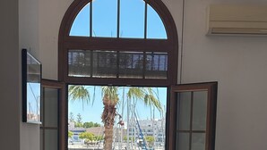 An open door leading to a balcony with a view of a marina, a chair, and a small table.
