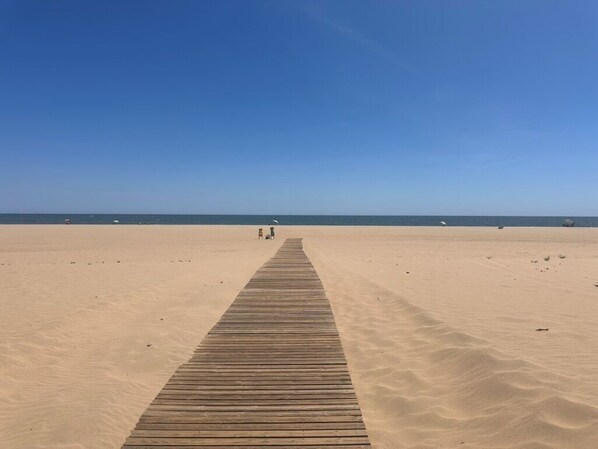 Ein Holzsteg führt zu einem Strand unter blauem Himmel.