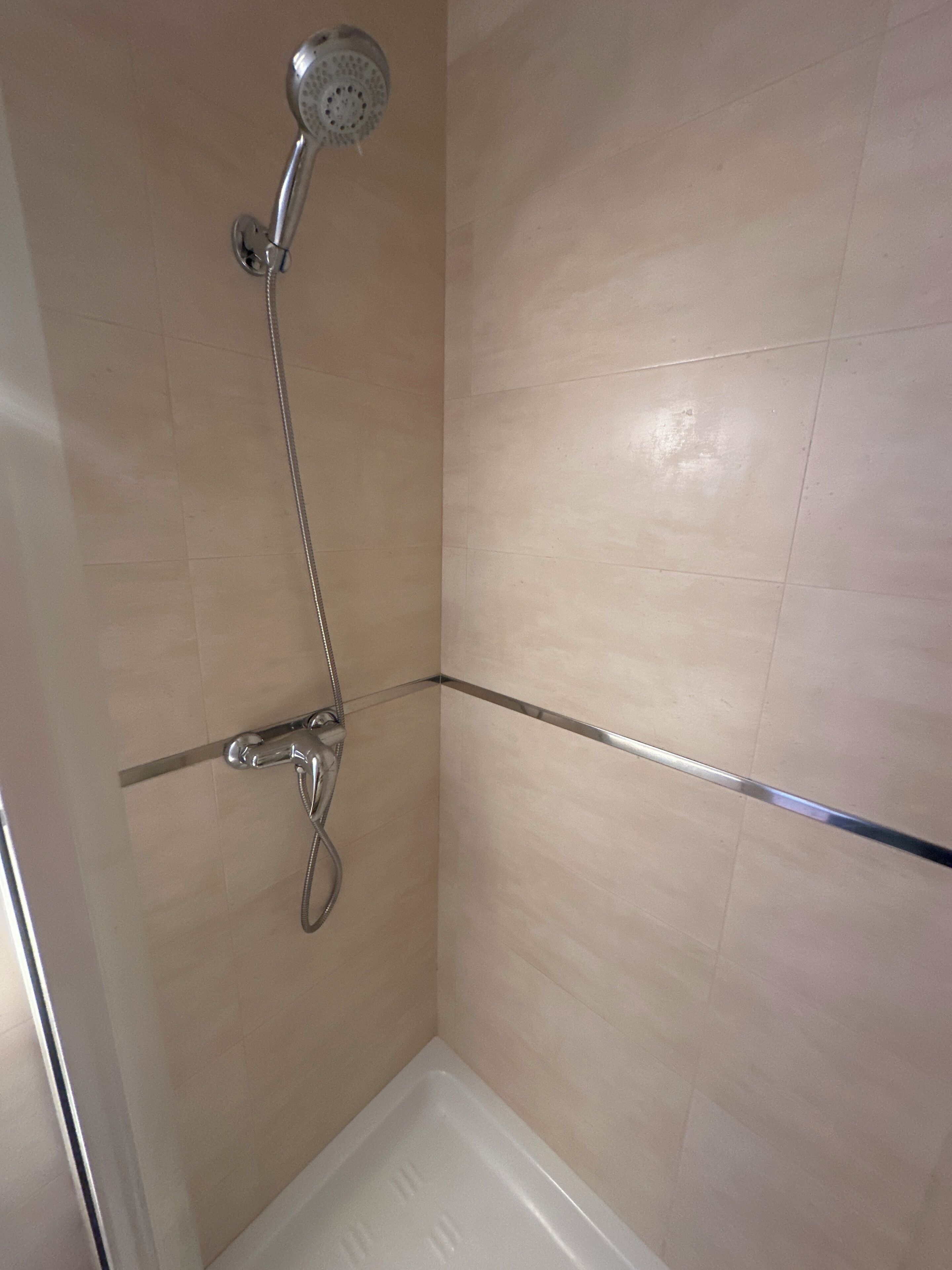 A shower with a handheld showerhead and a wall-mounted faucet, a corner tile shower enclosure, and a clear shower curtain rod.