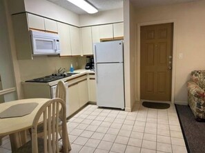 A compact kitchen with a microwave, stove, refrigerator, and a dining table with chairs. - Beachfront Condo at Treasure Island Beach Club (Treasure Island)