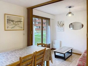 Ein Essbereich mit Tisch, Stühlen, einem Heizkörper, einer Hängelampe und einem Fenster mit Blick auf ein Gebäude.