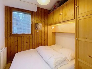 Ein Zimmer mit Holzwandverkleidung, einem Bett mit weißer Bettwäsche, einem Fenster mit Jalousien und einer Deckenleuchte.