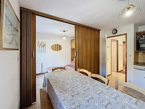 Une pièce comprenant un lit, une table à manger, des chaises, une armoire en bois, un coin cuisine et un luminaire au plafond.