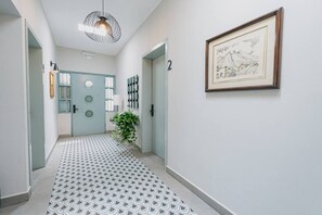 A hallway with a patterned floor, a door with a circular window, a wall-mounted light fixture, and a framed picture. - Loft con entrada 24/7 | Check-in autónomo (Monterrey)