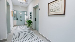 Ein Korridor mit einem gemusterten Boden, einer Tür mit rundem Fenster, einer Wandleuchte und einem gerahmten Bild.