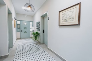 Ein Korridor mit einem gemusterten Boden, einer Tür mit rundem Fenster, einer Wandleuchte und einem gerahmten Bild.