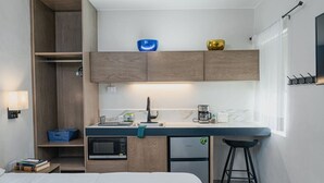 Ein kompaktes Hotelzimmer mit Küchenzeile, einem Bett, einem kleinen Tisch und einem Fenster.
