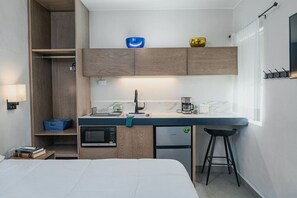 Pieni hotellihuone, jossa on minikeittiö, sänky, pieni pöytä ja ikkuna.