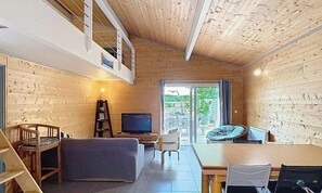 Ein Holzinterieur mit einer Couch, einem Fernseher, einem Esstisch und Stühlen.