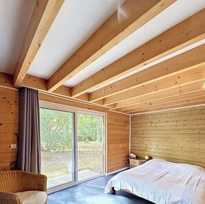 Ein Schlafzimmer mit großem Fenster, Holzbalkendecke und einem Bett.