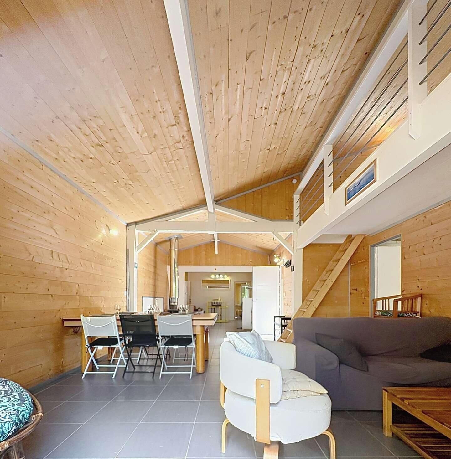 A spacious room with a high ceiling, wooden walls, a dining area with chairs and a table, and a sofa.